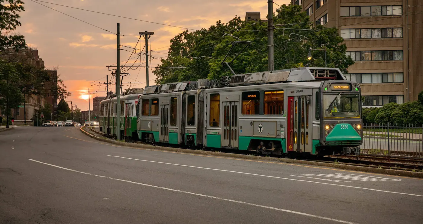 A Green Line trolley rolling down the tracks at sunset