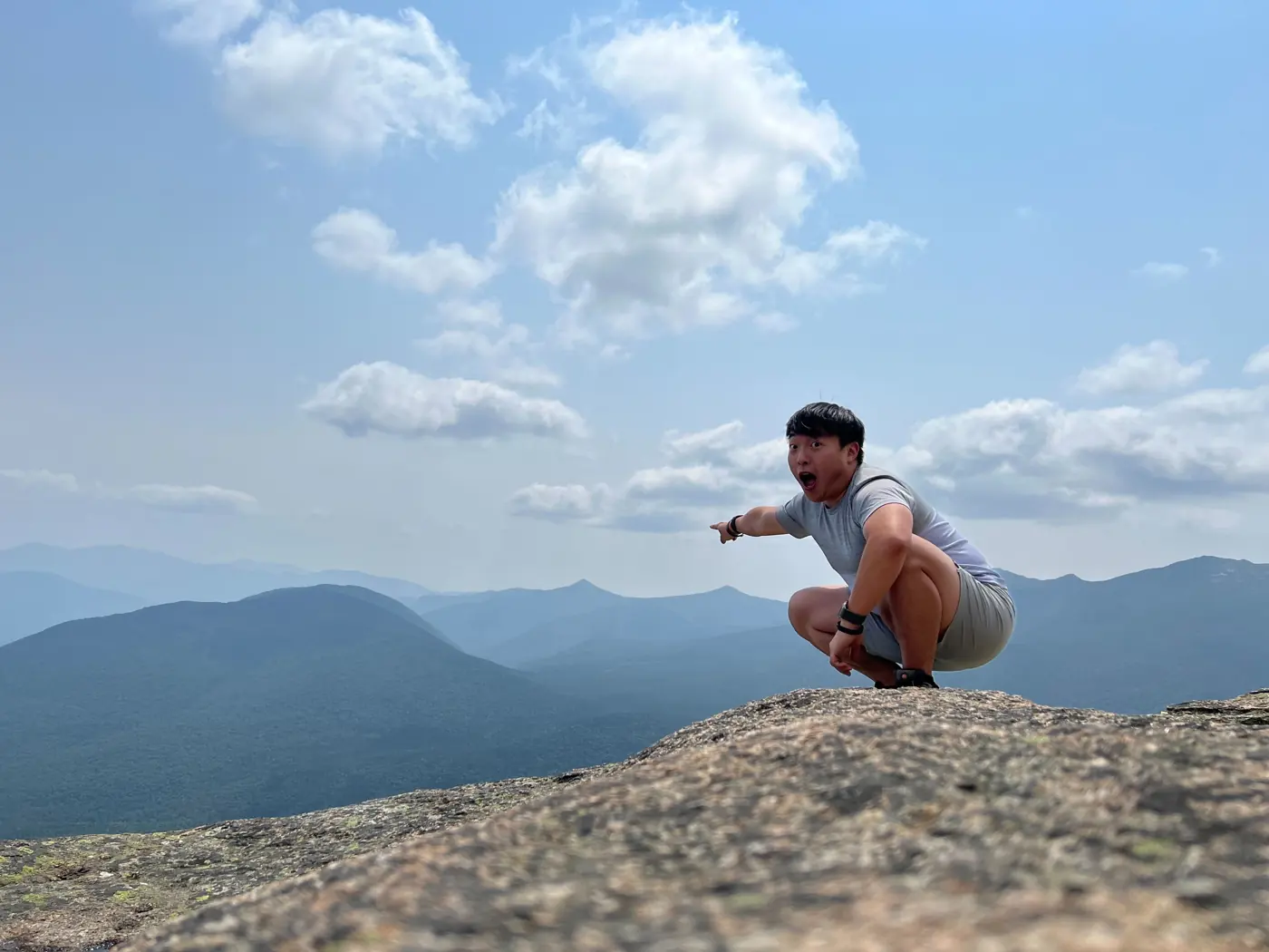 Will crouching on a rocky summit above layers of mountains